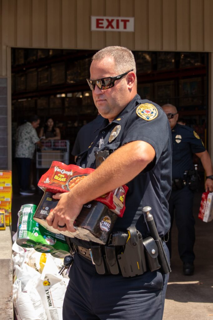 Officer carrying cases of canned food during food drive.