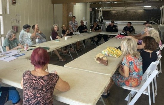 Group of seniors around a table talking with police officers with man raising hand in air. 