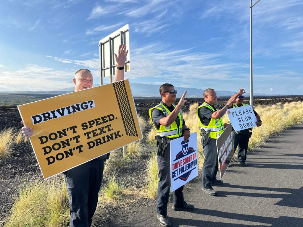 Officers waving to motorists during roadside sign waving event to promote traffic safety.