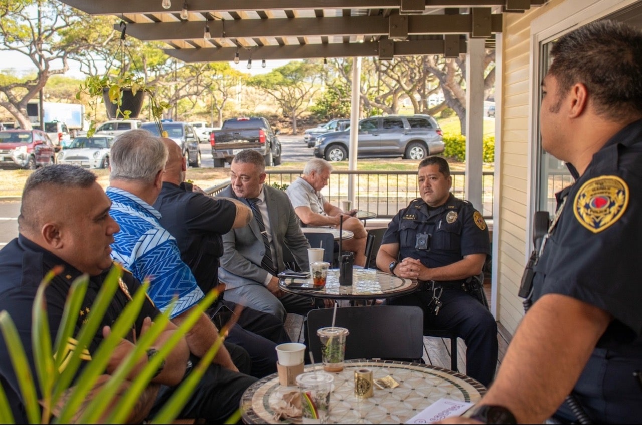 Officers seated on coffee shop lanai talking with people during Coffee With a Cop.