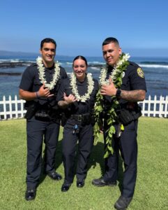 Pictured left to right: Officers Dallas Arce, Shaneil Azevedo, and Ashton Gomes on a grassy area with ocean in the background.