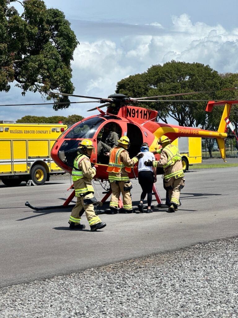 Firefighters assisting injured woman onto helicopter.