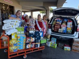 Three people behind stacks of food next police cruiser during police food drive in Kona. 