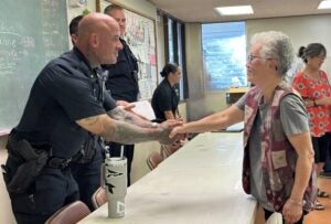 Picture of police officer shaking elderly woman’s hand at senior citizens community meeting.