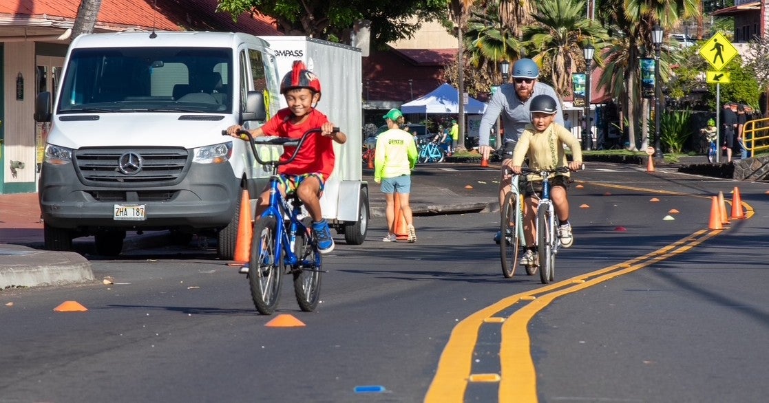 Two kids bicycling down street during 2026 Kona Bike Day event in Kona.