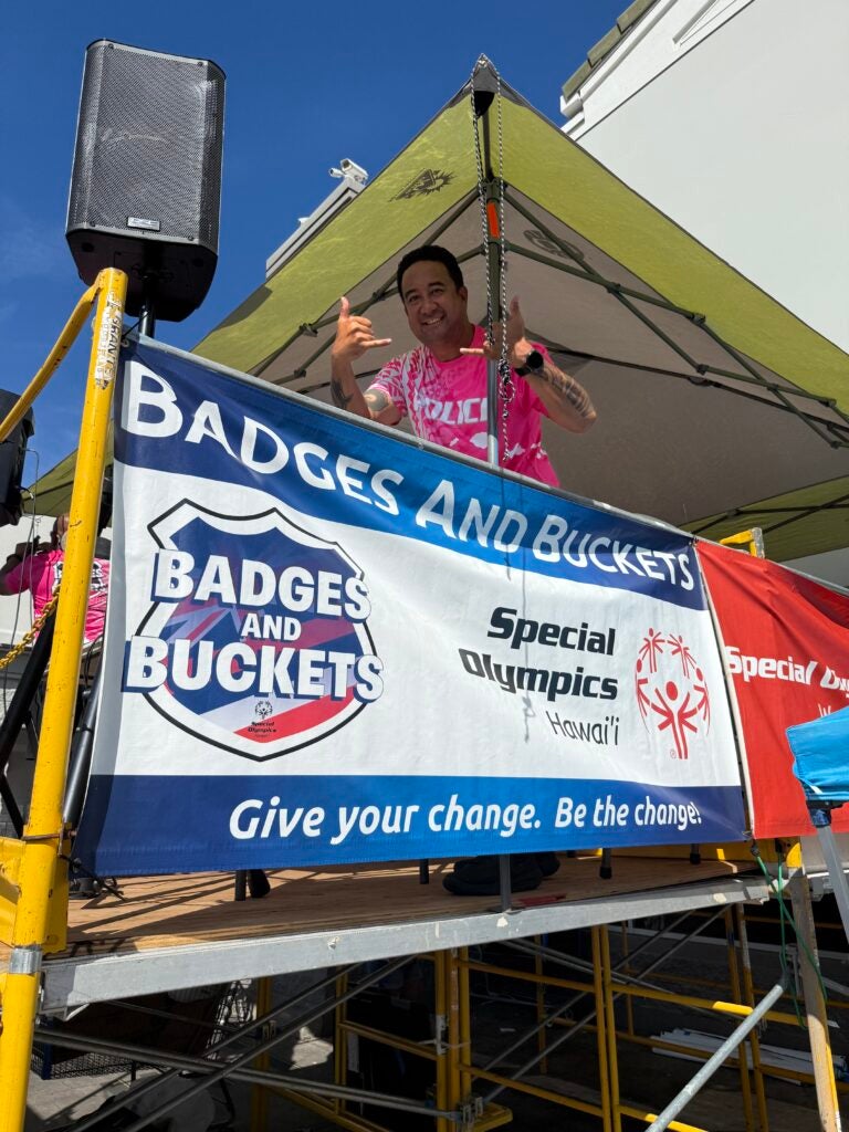 Officer on top of scaffolding smiling with banner for Special Olympic Hawaii.