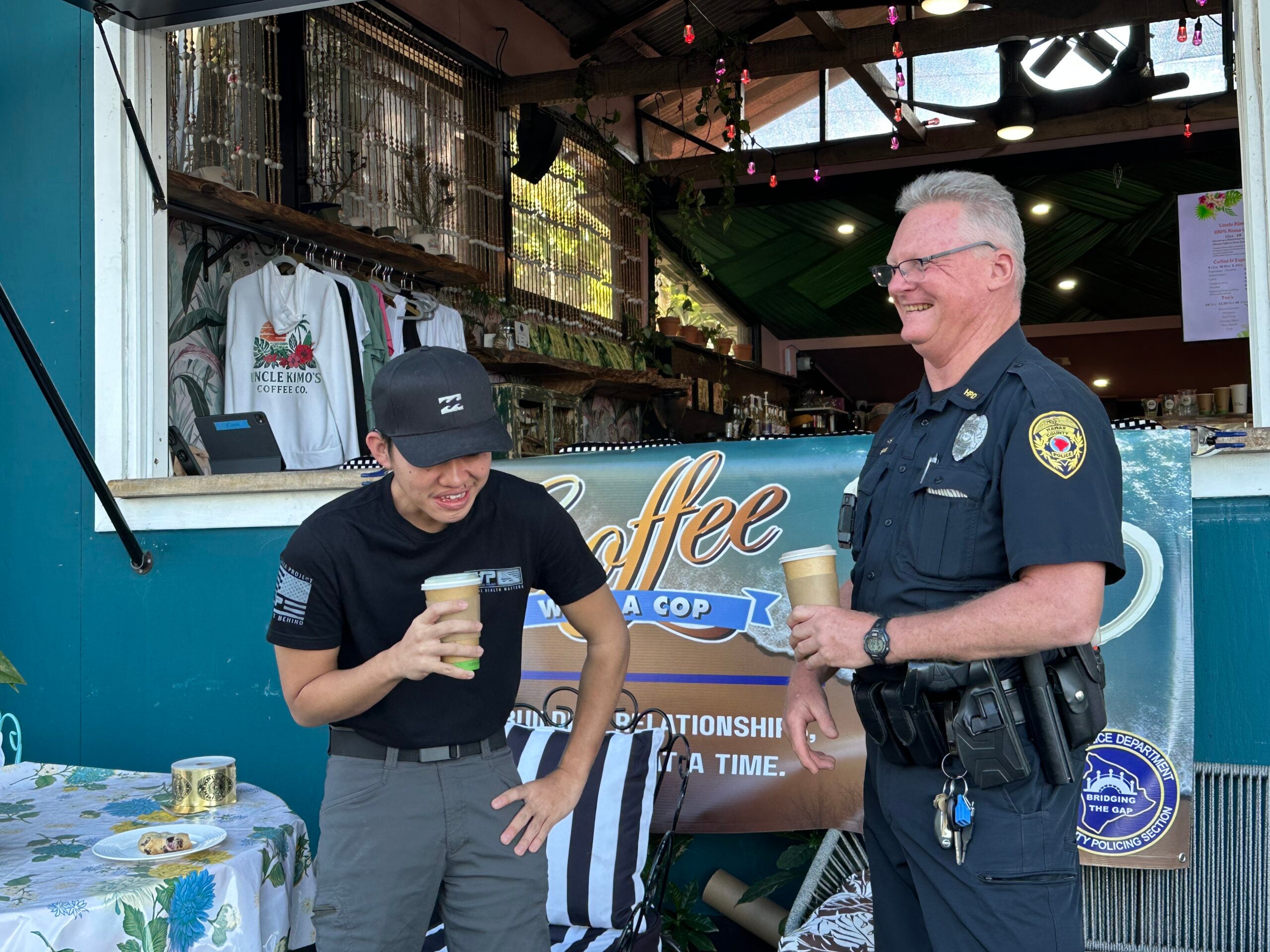 Young man and Ofcr Sluss laughing in front of coffee cafe.