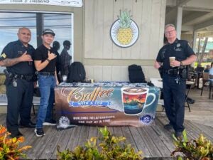 Two officers and young man next to Coffee With a Cop banner at coffeehouse.