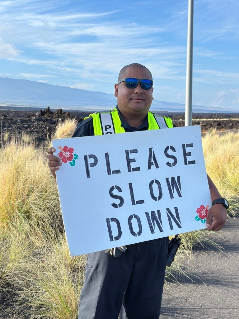 Officer Justin Cabanting holding sign saying "please slow down" during traffic safety awareness event in Waikoloa October 29, 2025.