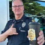 Officer Sluss holding out a cup of coffee during Coffee With a Cop event.