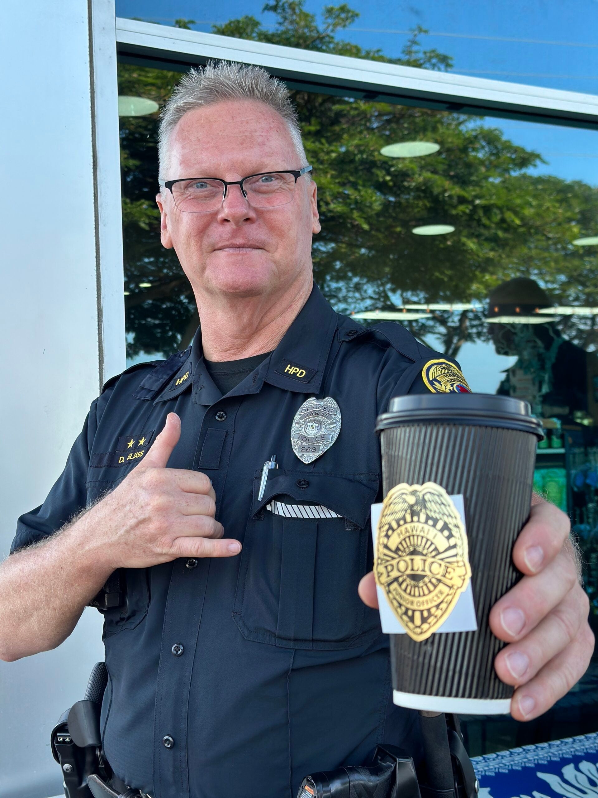 Officer Sluss holding out a cup of coffee during Coffee With a Cop event.
