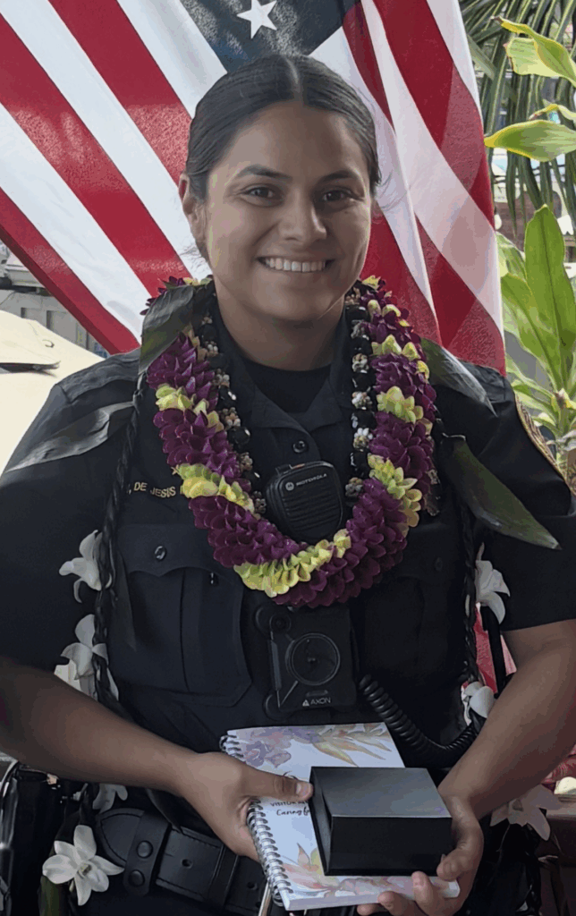 Kona Patrol Officer Victoria Dejesus-Monteiro in uniform and wearing lei around her neck holding her award for Kona Crime Prevention Committee’s Officer of the Month for August 2025.
