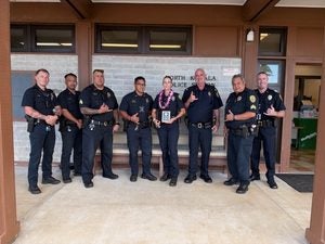 Seven police officers posing with Officer Jessica Cook who is holding her Officer of the Quarter award. 