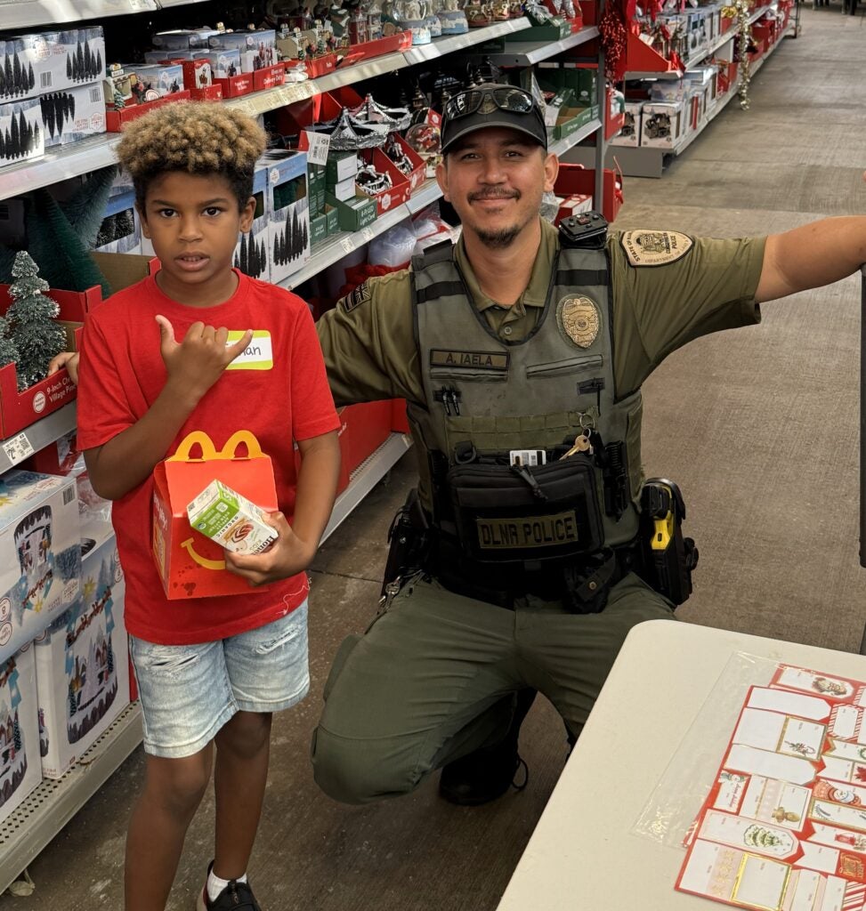 Department of Land and Natural Resources DOCARE officer with young boy during Shop With a Cop.