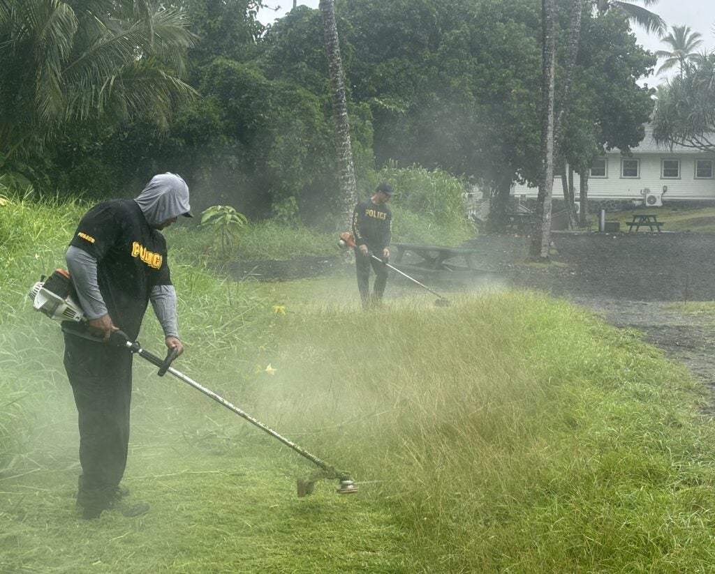 Two officers weed whacking at beach clean up.