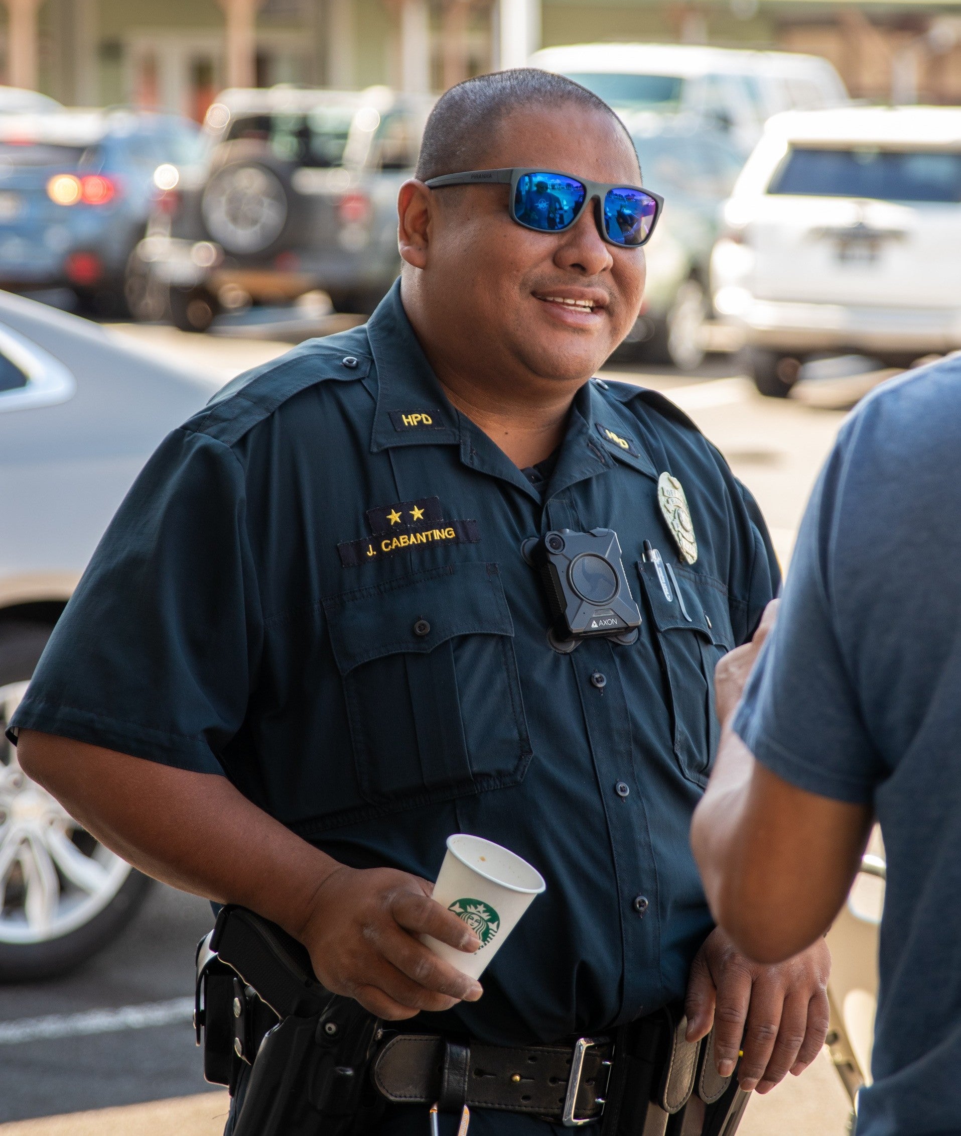 Officer Justin Cabanting holding a cup of coffee and talking to a man.