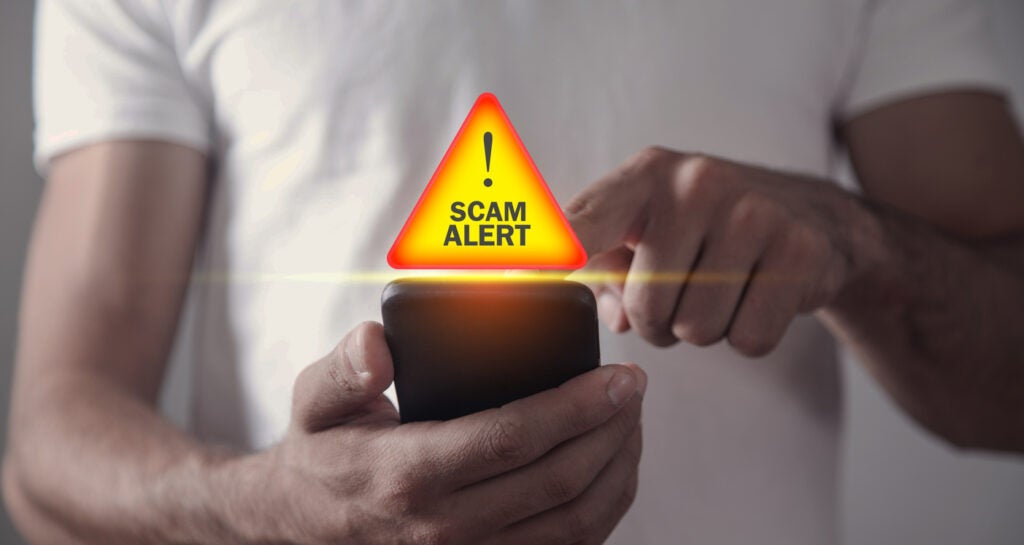 Man holding smartphone with text Scam Alert